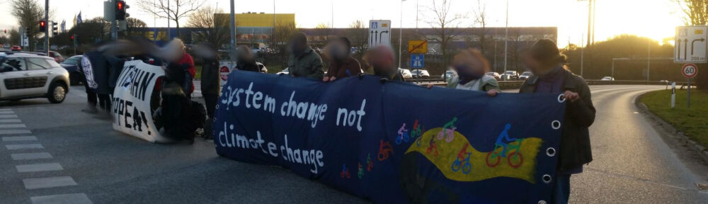 Menschen stehen auf der Straße und halten ein Transparent "System change not climate change"